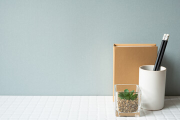 Working desk with notebook, pencil holder, potted plant on white tile desk. gray wall background