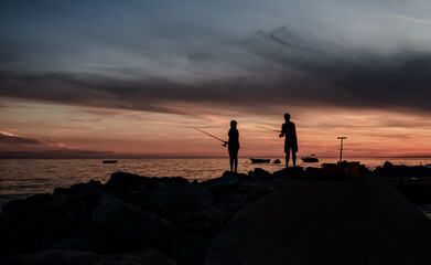Dwoje wędkarzy dziewczyna i chłopak, sylwetki osób, zachodzące słońce nad brzegiem morza,...