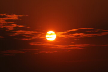 a dark orange sky with clouds veils through the sun during a sunset in summer