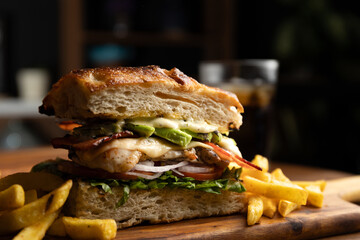 Grilled chicken breast sandwich with lettuce, tomato, bacon, red onion rings and avocado served on artisan bread and a portion of French fries - obrazy, fototapety, plakaty