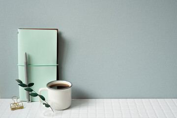 Workspace with diary notebook, pen, coffee on white tile desk. gray wall background