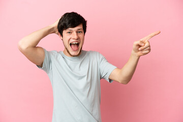 Young Russian man isolated on pink background surprised and pointing finger to the side