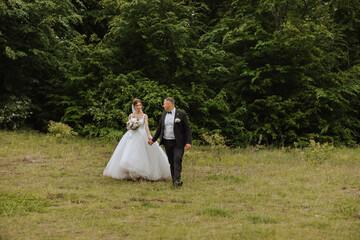 Portrait of a young bride and groom walking on green grass in a large field after the wedding ceremony, front view. Happy wedding couple, copy space