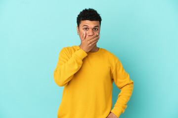 Young African American man isolated on blue background covering mouth with hand