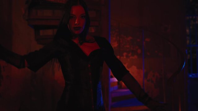 A gorgeous girl in a total black Halloween costume playing with fireworks near the stairs with candles. Sparkle in her hand. Nighttime, outdoor, slow motion. 