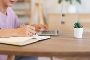Female entrepreneur working at home to searching business data on laptop and writing notes in paper