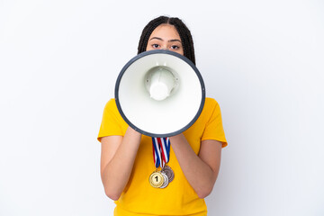 Teenager girl with braids and medals over isolated pink background shouting through a megaphone