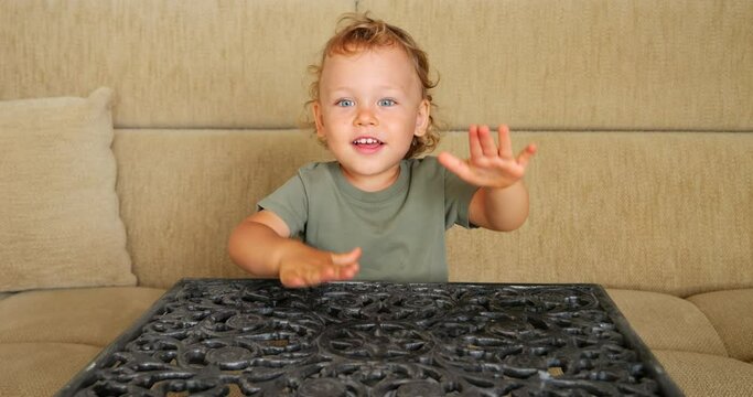 In this cheerful and frolicsome scene, baby boy sits at openwork cast-iron table, playfully beating out rhythm with his hands. Slow-motion footage captures his joyful and energetic play