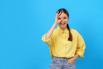 Women smile and doing gesture of ok sign on eye with empty space on isolated light blue background