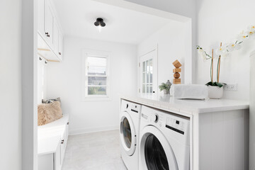 A remodeled laundry room and mud room with new appliances, tiled floor, and bench with cabinets above. No brands or logos. - obrazy, fototapety, plakaty