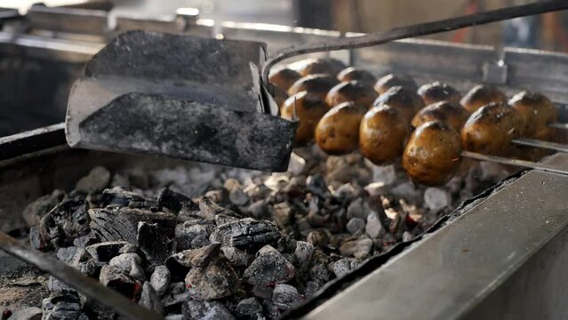 Close-up of a steel scoop filled with hot charcoal, pour the coals into the grill for frying kebabs, shish kebab and whole grilled potatoes. Cooking fried meat using hot coals