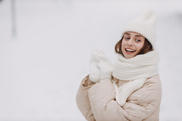 Happy smiling young woman portrait dressed coat scarf hat and mittens enjoys winter weather at snowy winter park.