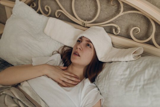 Young woman with headache flu ill sick disease cold at home indoor lying on bed with cold compress on her head at bedroom home