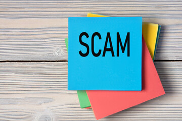 SCAM - word on note paper on wooden light background