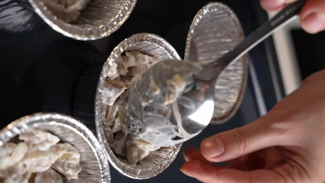 Julienne recipe baked with champignons and chicken in a creamy sauce, step-by-step preparation. Nutrition concept. Chef puts the filling into baking molds, tartlets in home kitchen.Vertical shot