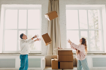 Happy young family couple man and woman throws cardboard boxes on new home. Moving delivery concept. - obrazy, fototapety, plakaty