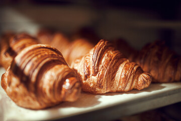 Close up photo of tray of golden brown, flaky and look freshly baked croissants in bakery. Dessert...