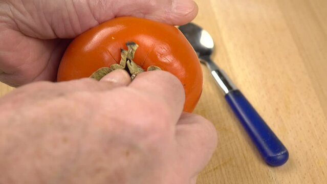 Person eats the flesh of whole persimmon with a spoon