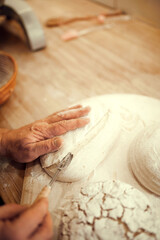 Chef, person's hand cutting through piece of dough with serrated knife which lying on wooden cutting board well dusted with flour. concept of nature, food, diet, cooking, bakery, ingredients.