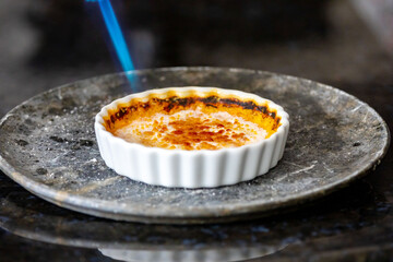 Crème brûlée, creme brule. Classic creme brulé being flambé. Burning, flaming, ramekins, vanilla beans, blowtorch, sugar