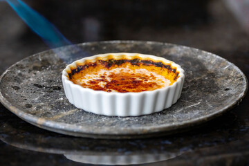Crème brûlée, creme brule. Classic creme brulé being flambé. Burning, flaming, ramekins,...