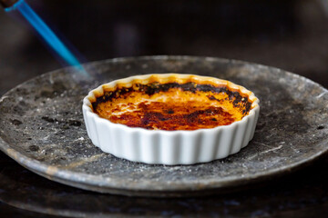 Crème brûlée, creme brule. Classic creme brulé being flambé. Burning, flaming, ramekins,...