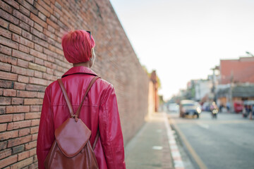 Fototapeta premium Gen z girl leather fashion with punk Asian woman tourist of local city Southeast Asia travel trendy pink hairstyle young female punk traveler walking around in town