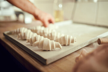 Chef's hands hands lay out sweet or savory pastries, croissant dough pieces on bakery plate covered...
