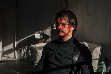 a tired man with a broken face covered in blood sits by the window. guy with makeup, cosplay