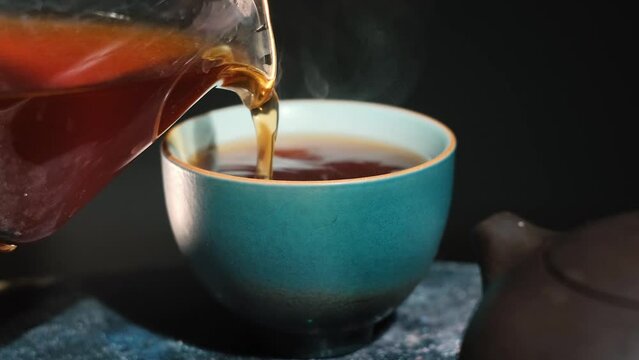 Pouring tea into a bowl. Chinese tea ceremony. Ceramic kettle. Close-up. Slow motion