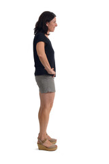 side view of a woman with shorts looking at camera and arms akimbo on white background