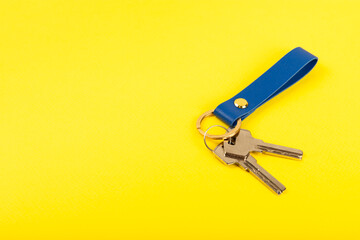 Leather keychain with a key ring on a yellow background. Concepts for real estate and moving home or renting property. Buying a property. Mock-up keychain.Copy space.