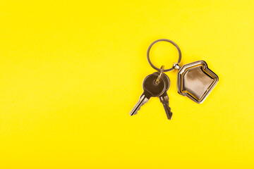 Keychain in the shape of a house with a key ring on a yellow background. Concepts for real estate...