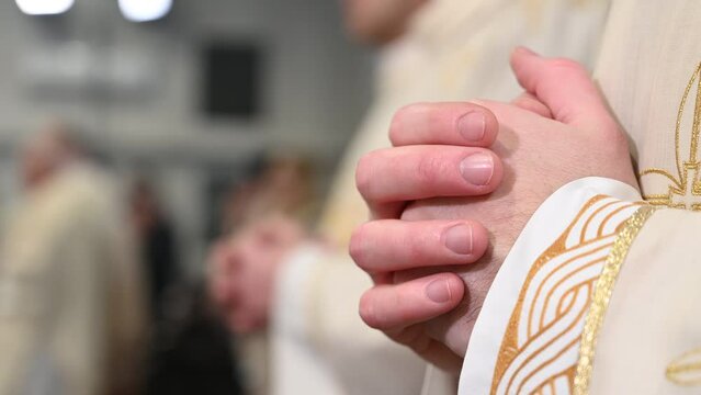Catholic priests in liturgical vestments praying with hands folded. Hands of Christian man praying in Cathedral. Christmas Midnight Mass in church.  