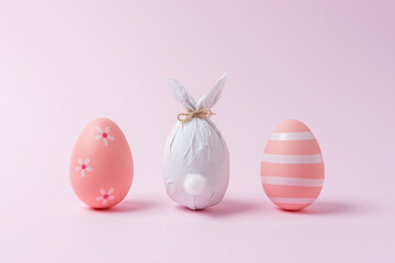 Easter egg wrapped in a paper in the shape of a bunny with colorful Easter eggs. Minimal Easter concept.