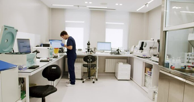 Man laboratory assistant analyzing blood sample and determinate type and rhesus at modern clinic with medical equipment. Male lab technician working at hospital. Biochemistry research concept