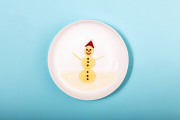 Beautiful snowman figure made of cheese, beetroot and peppercorns on white plate on blue...