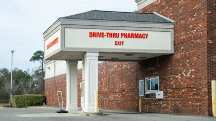 Drive-thru pharmacy exit with red signage on a brick building, covered drive-up window, and a clear day.
