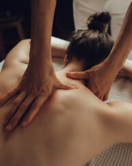 Hands of female chiropractor massaging shoulders of young woman lying on massage table. Concept of...