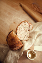 Pieces of just prepared, delicious, hot homemade loaf of bread with golden brown crispy crust lying in natural fabric on wooden table with honey in small plate. Concept of tradition and innovation.