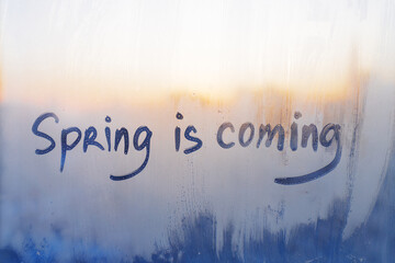 lettering Spring is coming on foggy glass on blue sunset window