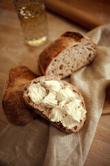 Photo in selective focus. Pieces of delicious, hot homemade loaf of bread with fresh homemade butter lying in natural fabric on wooden table. Concept of food, bakery, tradition and innovation, recipe.