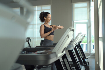 Happy healthy hispanic woman practicing a cardio exercise by running and walking on treadmill...