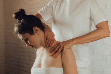 Hands of female chiropractor massaging shoulders of young woman lying on massage table on white...
