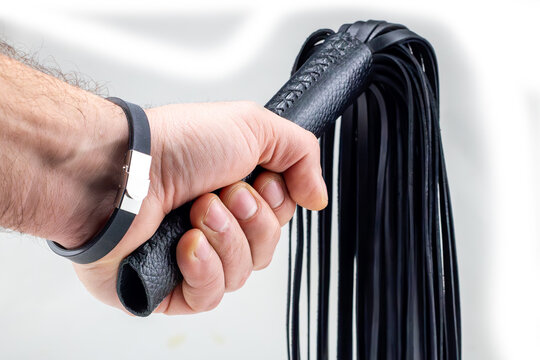 BDSM concept. A man's hand holds a black flogger on a white background. Isolated.