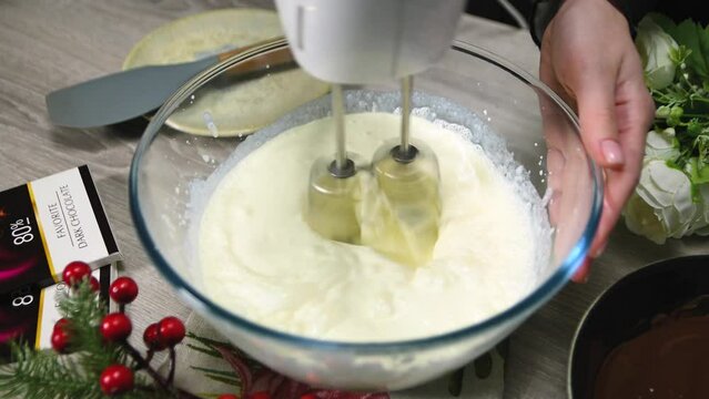 Woman whipping cream in a glass bowl with a mixer in the kitchen. Whipped cream cheese dessert