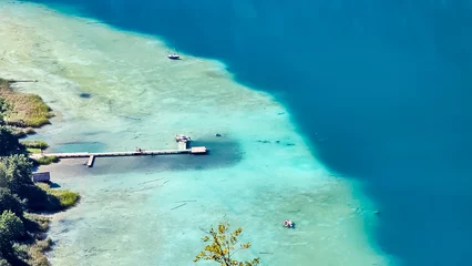 Papier Peint photo Plage de Camps Bay, Le Cap, Afrique du Sud Aerial view of east bank of alpine lake Weissensee in Carinthia, Austria. Wooden pier in turquoise water of bathing lake. Remote untouched nature in summer. Vacation vibes. Boats floating in the bay