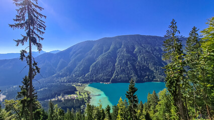 Naklejka premium Aerial view of east bank of alpine lake Weissensee in Carinthia, Austria. Pristine turquoise water of bathing lake. Tranquil forest in serene landscape in remote untouched nature in summer. Vacation