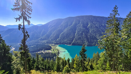 Aerial view of east bank of alpine lake Weissensee in Carinthia, Austria. Pristine turquoise water of bathing lake. Tranquil forest in serene landscape in remote untouched nature in summer. Vacation