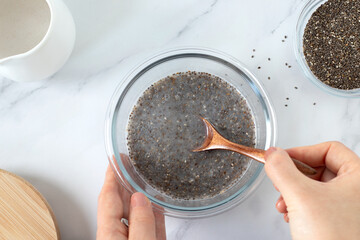 Hands holding and preparing a bowl chia seed pudding with plant-based milk in the kitchen. Top...